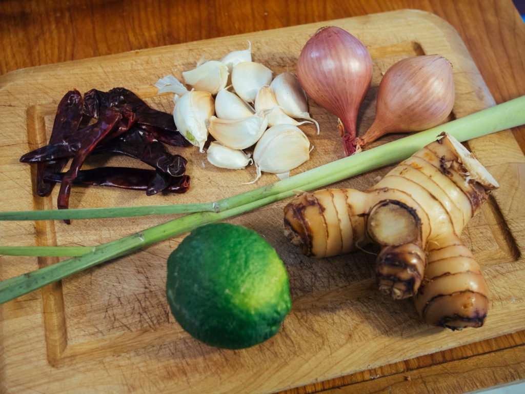 getrocknete Chillies, Knoblauch, Schallotten, Zitronengras, Limette und Galgant auf Holzbrett