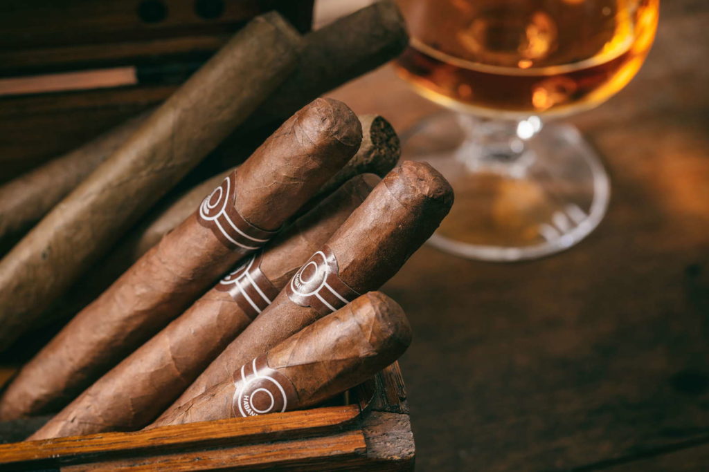 Zigarren in einer Holzkiste, im Hintergrund ein Glas mit Cognac