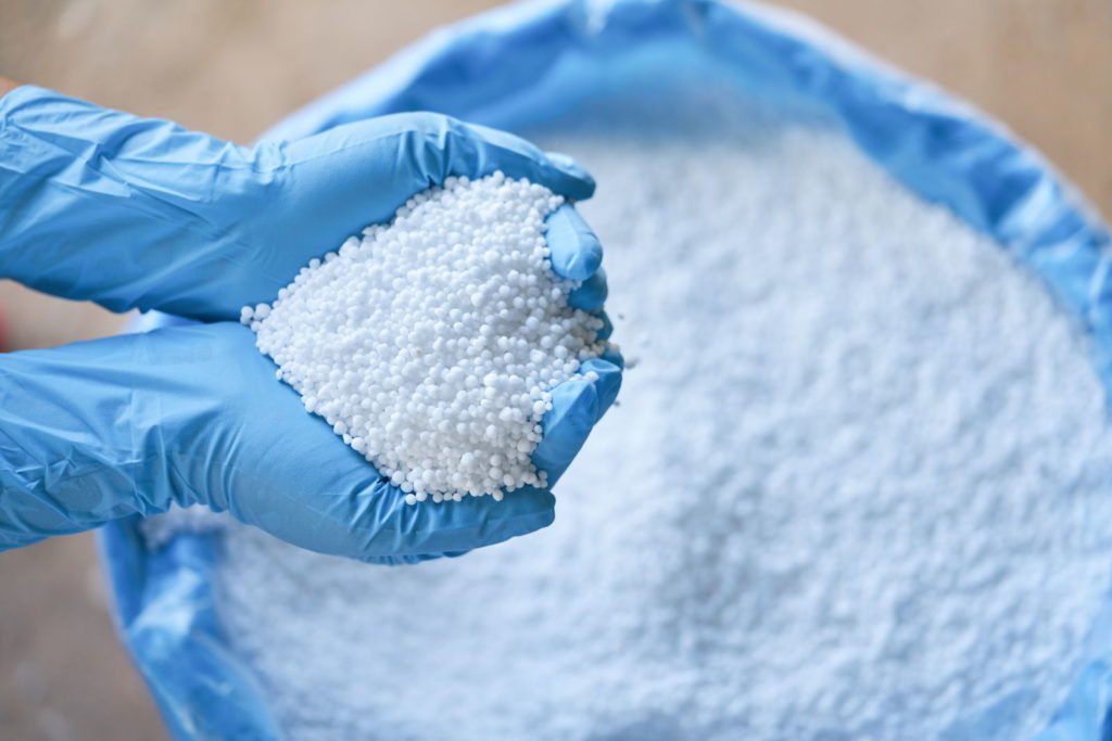 Weißer Dünger in Händen mit blauen Handschuhen