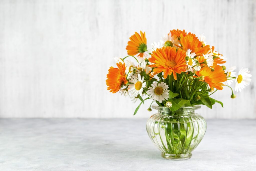Vase mit Ringelblumen und Gänseblümchen